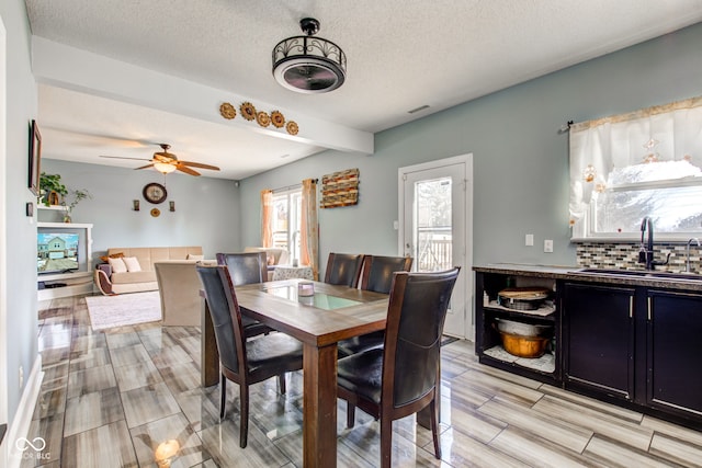 dining area featuring beamed ceiling, ceiling fan, sink, and a textured ceiling