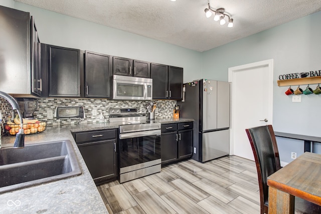 kitchen with sink, light hardwood / wood-style flooring, a textured ceiling, appliances with stainless steel finishes, and backsplash