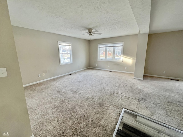 carpeted empty room with ceiling fan, a textured ceiling, and a wealth of natural light