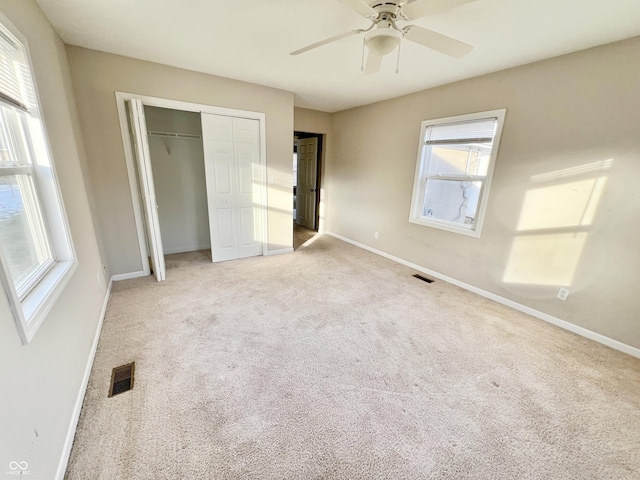 unfurnished bedroom with a closet, ceiling fan, light colored carpet, and multiple windows