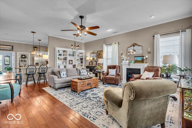 living room with ceiling fan with notable chandelier, wood-type flooring, crown molding, and a wealth of natural light