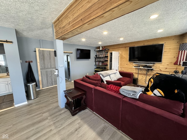 living room with a textured ceiling, wood walls, light hardwood / wood-style flooring, and a barn door