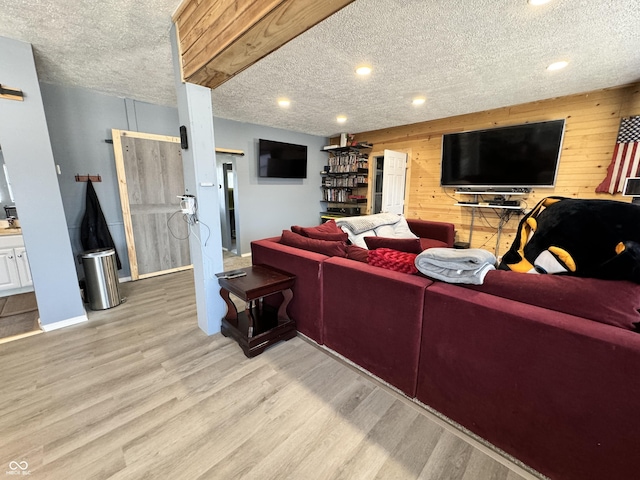 living room with a textured ceiling, light hardwood / wood-style floors, wooden walls, and a barn door