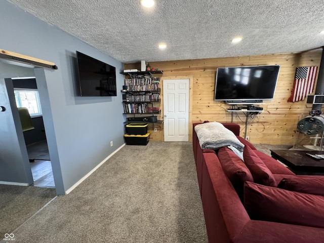 carpeted living room featuring a barn door, wood walls, and a textured ceiling