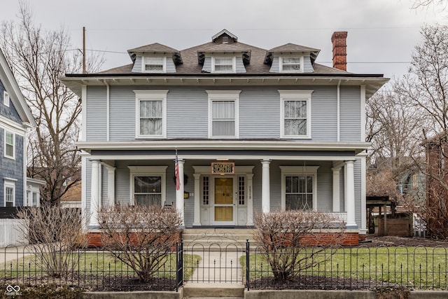 american foursquare style home featuring a fenced front yard, a chimney, a porch, and a front lawn