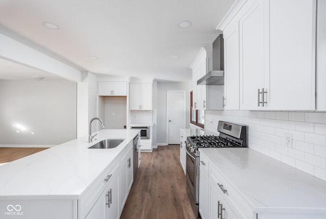 kitchen with appliances with stainless steel finishes, white cabinetry, an island with sink, sink, and wall chimney range hood