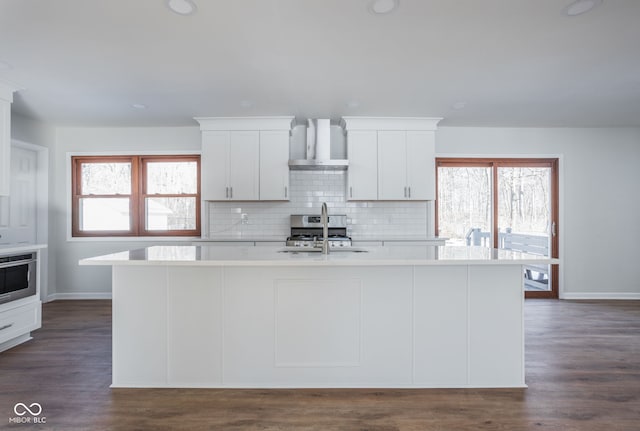 kitchen with wall chimney exhaust hood, sink, white cabinetry, an island with sink, and decorative backsplash