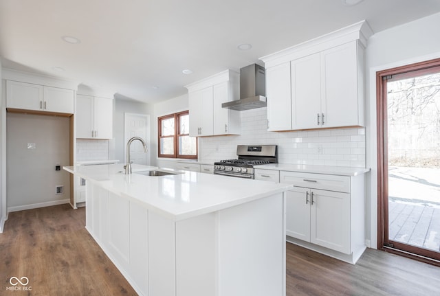 kitchen featuring sink, white cabinets, a kitchen island with sink, stainless steel gas range, and wall chimney exhaust hood