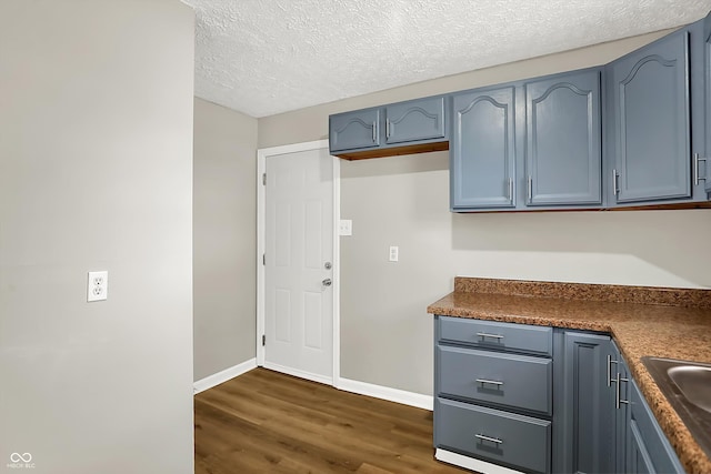 kitchen featuring a textured ceiling, blue cabinets, and dark hardwood / wood-style flooring