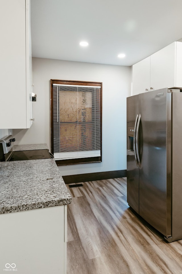 kitchen with white cabinetry, appliances with stainless steel finishes, light stone counters, and light wood-type flooring