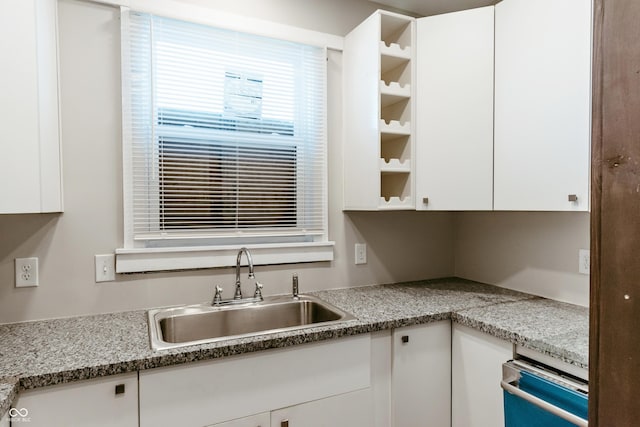 kitchen with light stone countertops, sink, and white cabinets