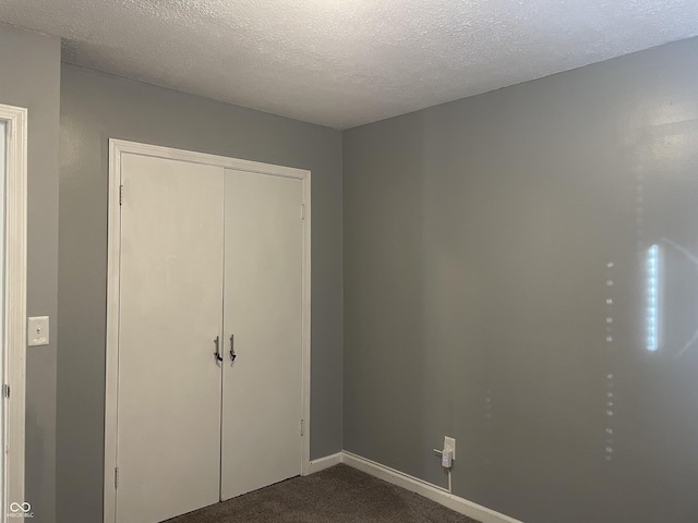 unfurnished bedroom with dark colored carpet, a textured ceiling, and a closet