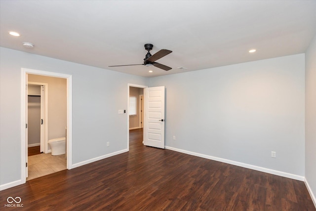 unfurnished bedroom with ceiling fan, a spacious closet, dark hardwood / wood-style floors, and ensuite bath