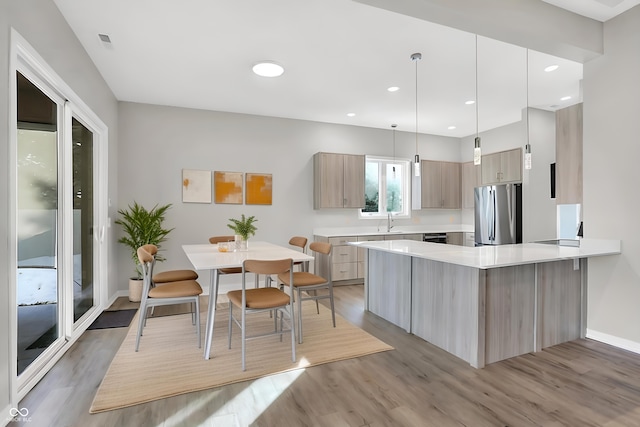 kitchen with sink, hardwood / wood-style flooring, stainless steel fridge, hanging light fixtures, and light brown cabinets