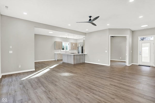 unfurnished living room featuring ceiling fan, sink, and hardwood / wood-style floors