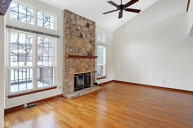 unfurnished living room with high vaulted ceiling, ceiling fan, wood-type flooring, and a stone fireplace