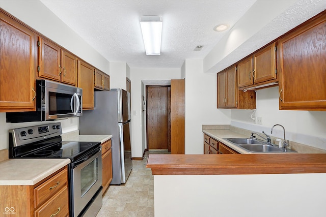 kitchen featuring sink, a textured ceiling, appliances with stainless steel finishes, and kitchen peninsula