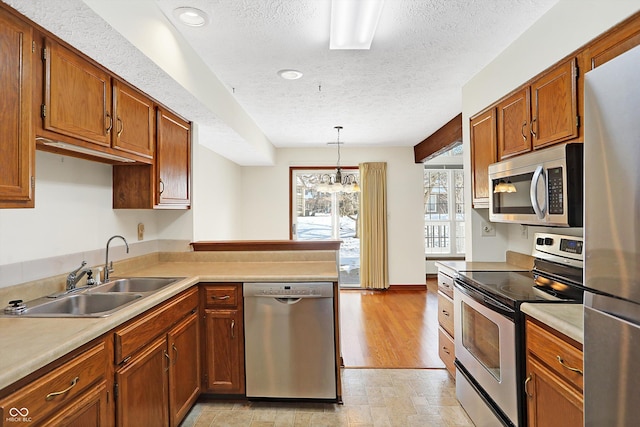 kitchen featuring a textured ceiling, hanging light fixtures, sink, kitchen peninsula, and stainless steel appliances