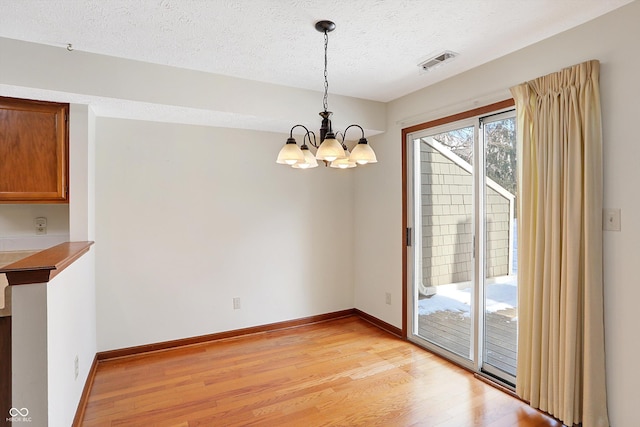 unfurnished dining area featuring a textured ceiling, a chandelier, and light wood-type flooring