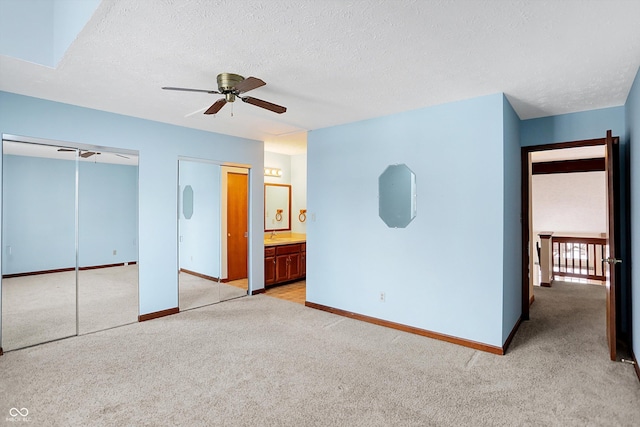 unfurnished bedroom featuring multiple closets, a textured ceiling, light colored carpet, ceiling fan, and connected bathroom