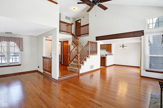 unfurnished living room featuring hardwood / wood-style flooring, a towering ceiling, and ceiling fan with notable chandelier