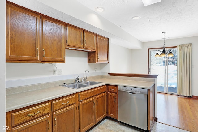 kitchen with a textured ceiling, stainless steel dishwasher, sink, decorative light fixtures, and kitchen peninsula