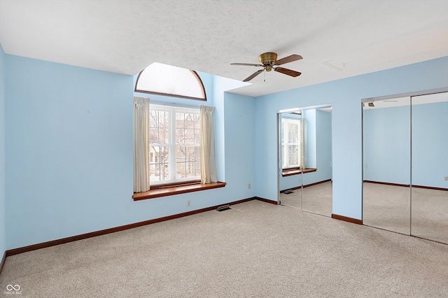 unfurnished bedroom featuring ceiling fan, two closets, and light carpet