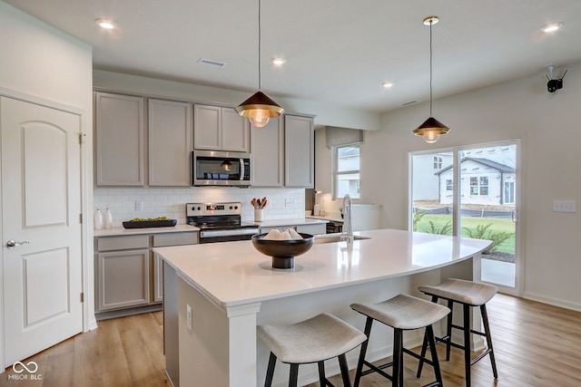 kitchen with pendant lighting, gray cabinets, stainless steel appliances, and an island with sink