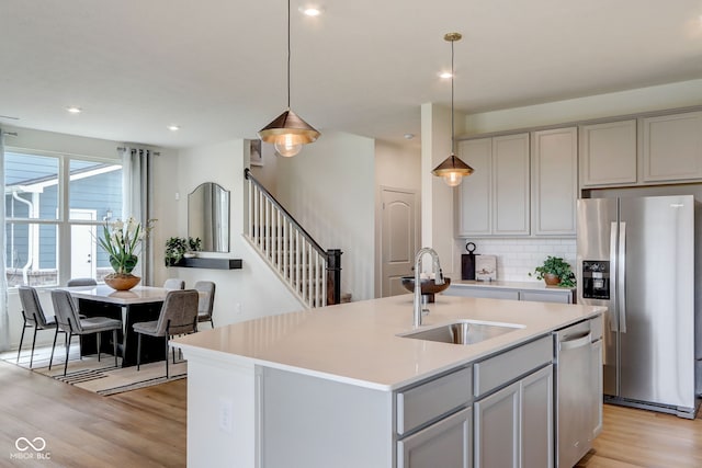 kitchen featuring hanging light fixtures, appliances with stainless steel finishes, sink, gray cabinets, and a kitchen island with sink