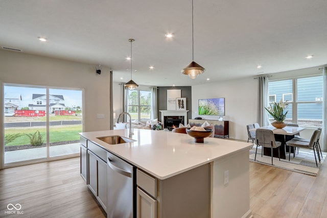 kitchen with dishwasher, a healthy amount of sunlight, an island with sink, sink, and hanging light fixtures