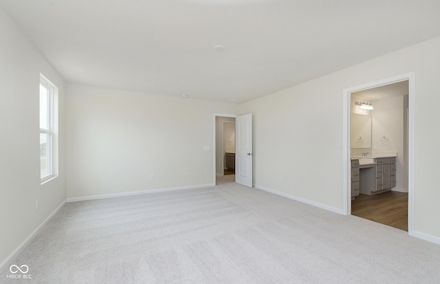 unfurnished bedroom featuring light colored carpet, ensuite bath, and baseboards