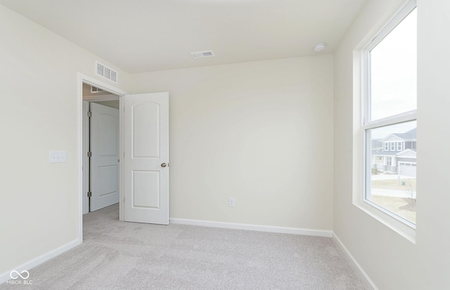 unfurnished bedroom with visible vents, multiple windows, light carpet, and baseboards