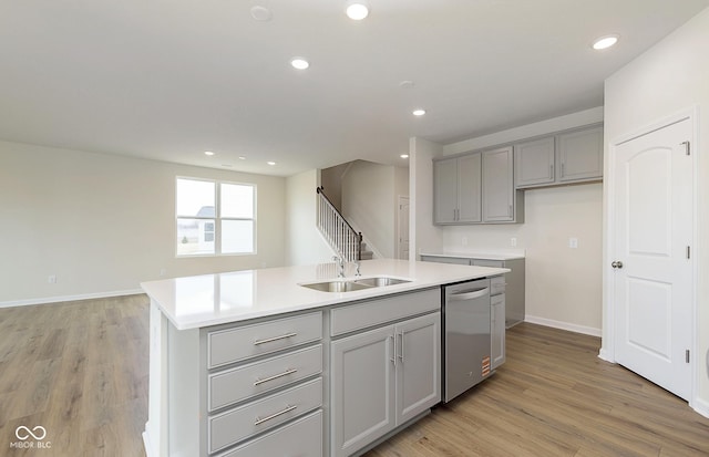 kitchen featuring light wood-style floors, gray cabinets, a kitchen island with sink, and dishwasher