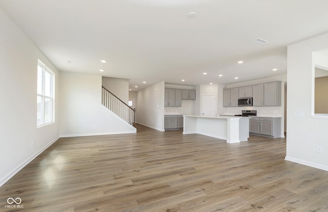 unfurnished living room featuring recessed lighting, baseboards, stairway, and light wood finished floors