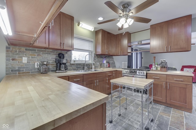 kitchen with wooden counters, tasteful backsplash, sink, kitchen peninsula, and stainless steel range with gas stovetop