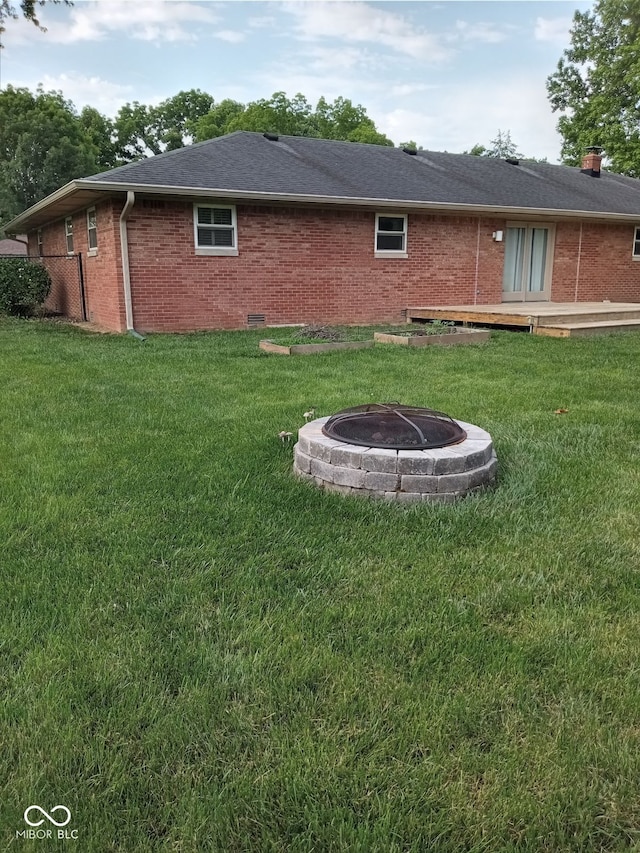 back of property with a wooden deck, an outdoor fire pit, and a yard