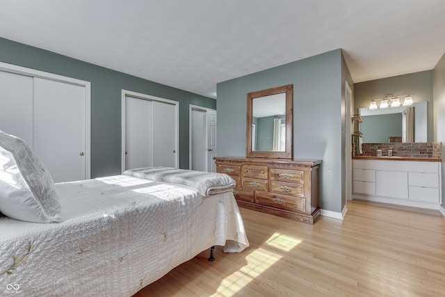 bedroom featuring sink, multiple closets, ensuite bath, and light wood-type flooring