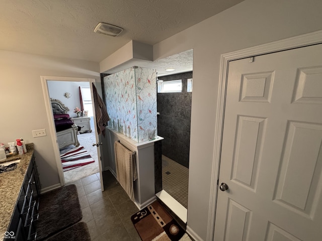 bathroom with tile patterned floors, tiled shower, vanity, and a textured ceiling