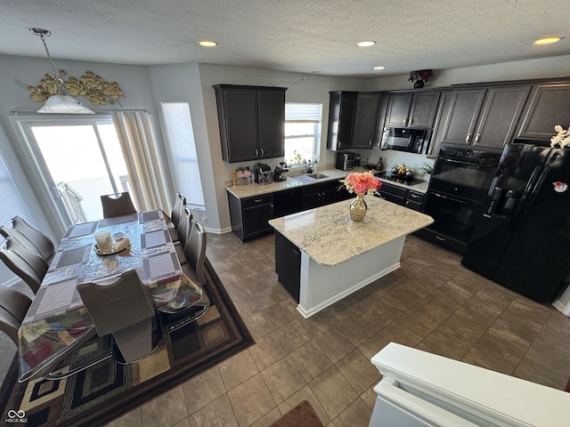 kitchen featuring black appliances, sink, a kitchen island, pendant lighting, and light stone counters