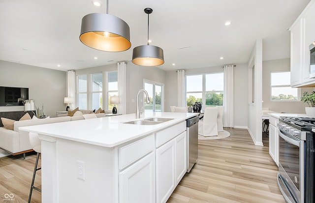 kitchen with white cabinets, stainless steel appliances, a kitchen island with sink, and decorative light fixtures