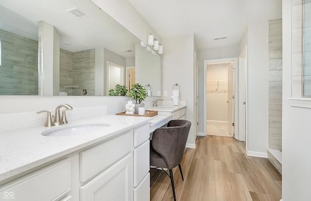 bathroom with wood-type flooring, a tile shower, and vanity