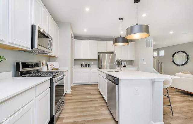 kitchen with decorative light fixtures, white cabinets, appliances with stainless steel finishes, and a kitchen island with sink