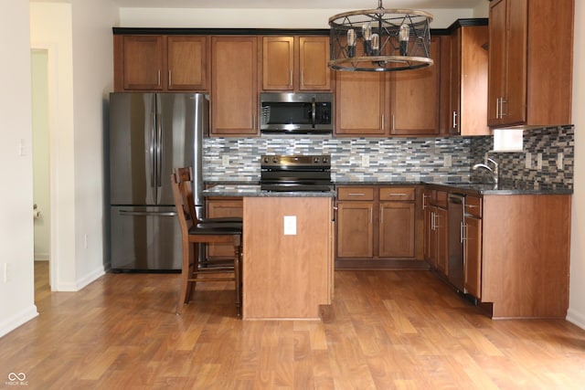 kitchen with sink, stainless steel appliances, a center island, decorative light fixtures, and light wood-type flooring