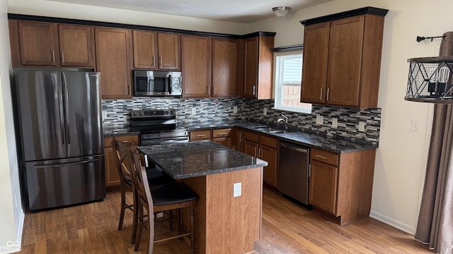 kitchen with a kitchen island, appliances with stainless steel finishes, sink, dark stone counters, and hardwood / wood-style flooring