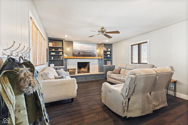 living room with a tile fireplace, ceiling fan, built in features, and dark hardwood / wood-style flooring