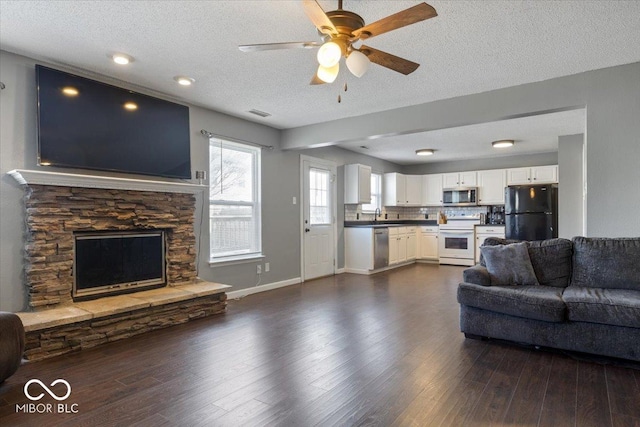 living room featuring ceiling fan, a stone fireplace, dark hardwood / wood-style flooring, and a textured ceiling