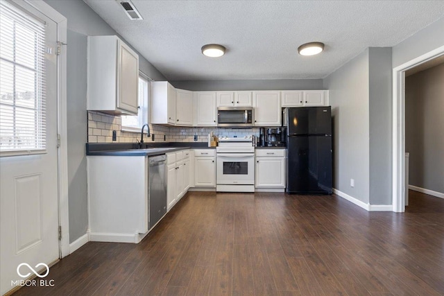 kitchen featuring appliances with stainless steel finishes, dark wood-type flooring, white cabinetry, decorative backsplash, and sink