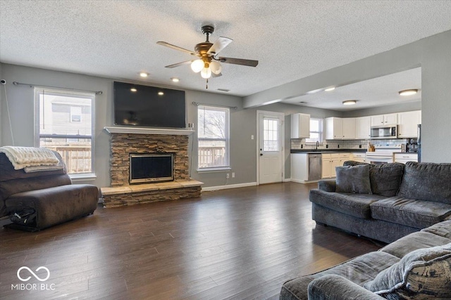 living room with a fireplace, a healthy amount of sunlight, a textured ceiling, and dark hardwood / wood-style floors