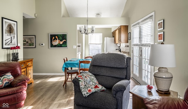 living area with hardwood / wood-style floors, lofted ceiling, a wealth of natural light, and a chandelier