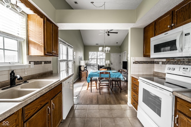 kitchen featuring sink, white appliances, light tile patterned floors, backsplash, and ceiling fan with notable chandelier